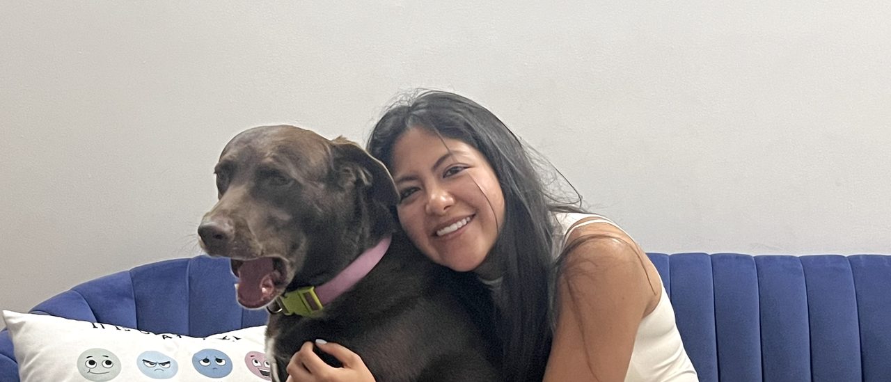 Una persona abraza a Oliva en el sofá del consultorio; las dos miran a la cámara
